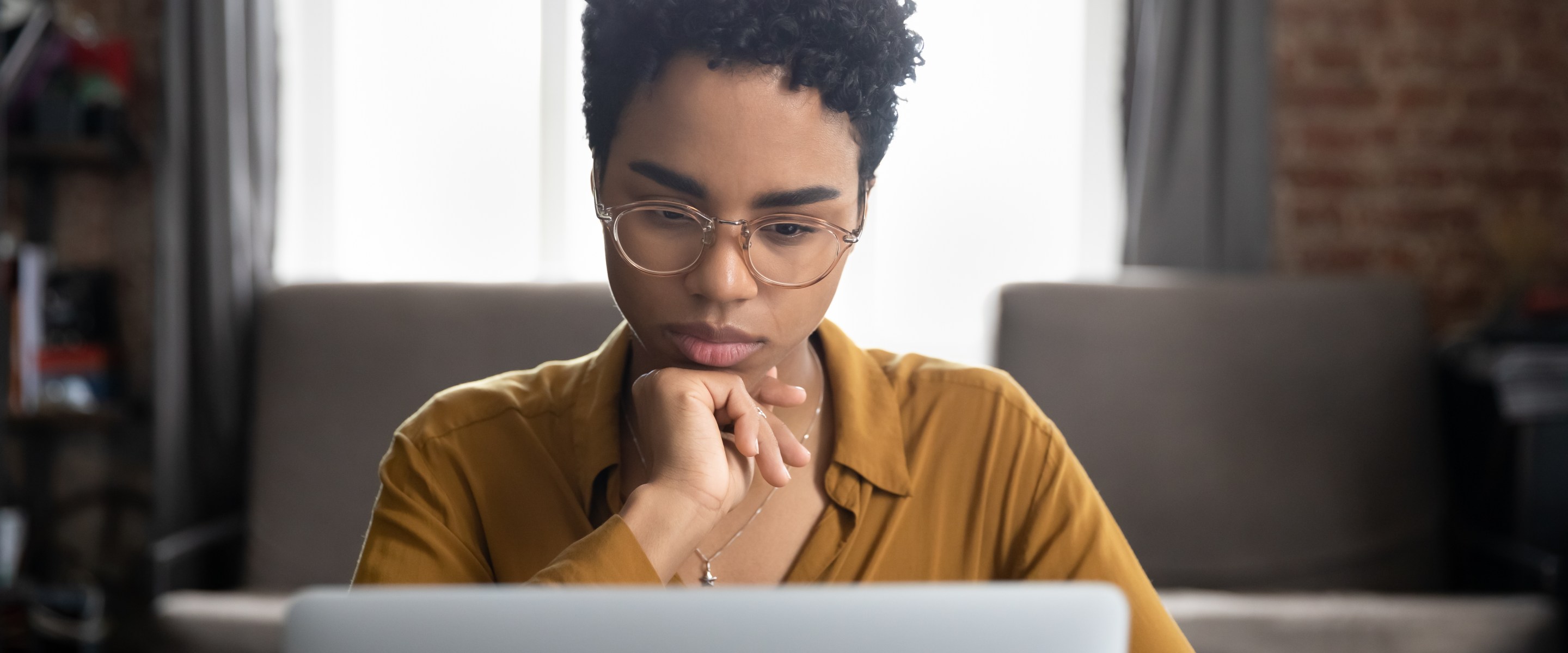 Young Black woman looking contemplative while using her laptop.