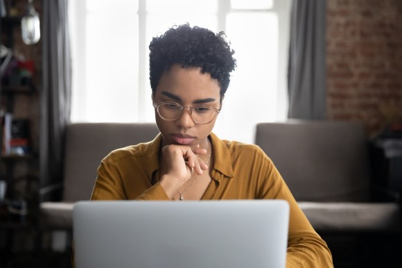 Young Black woman looking contemplative while using her laptop.