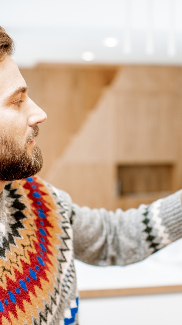 Man wearing a sweater adjusting thermostat.