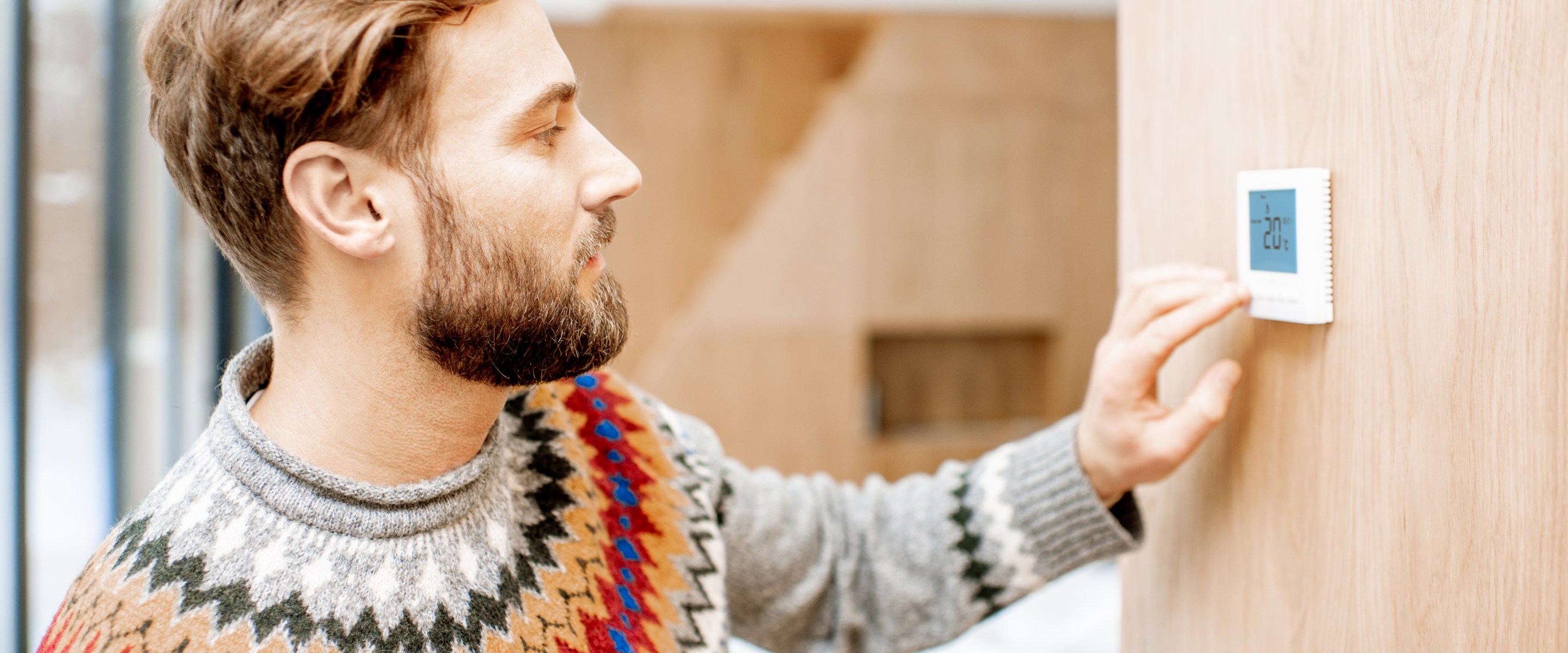 Man wearing a sweater adjusting thermostat.