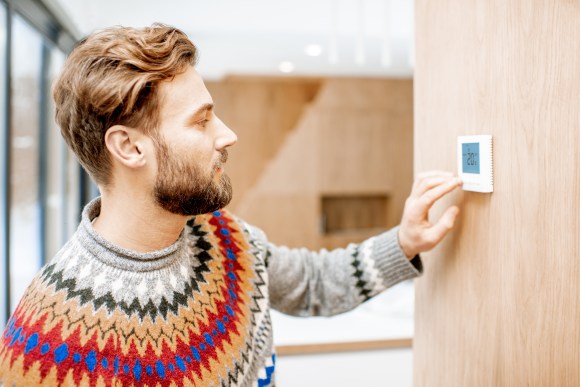 Man wearing a sweater adjusting thermostat.