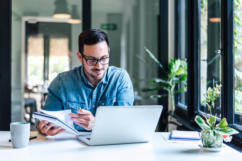 Young business owner reviewing documents and working on laptop.