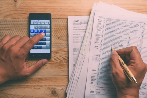 Closeup of a man’s hand as he uses his phone calculator and fills out Form 1040.