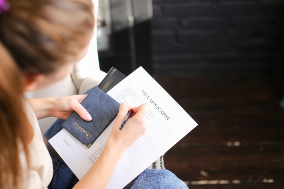 Close-up of a woman filling out a visa application and holding a passport.