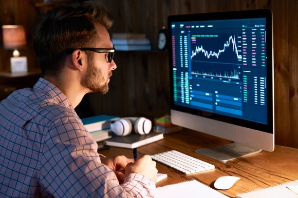 Young man analyzing investment performance and taking notes.