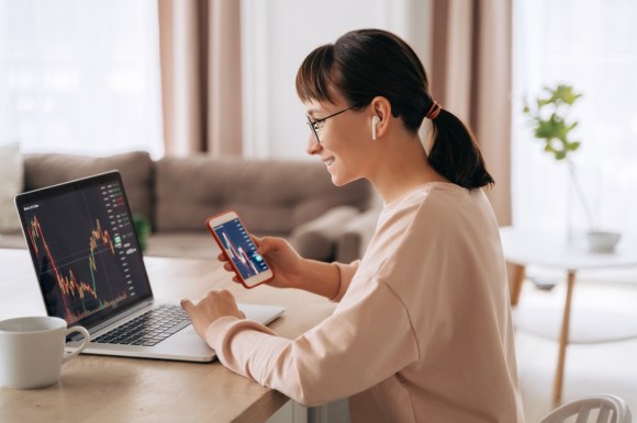 Young woman checking stock performance on her laptop and phone.