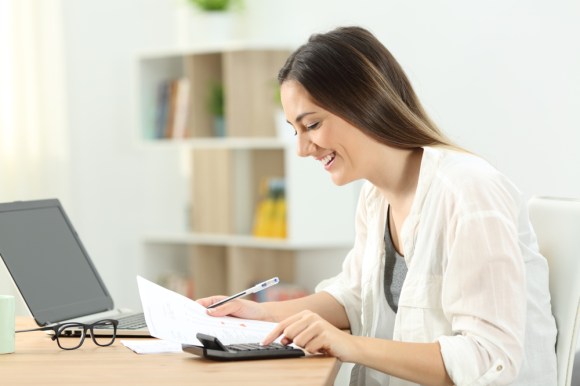 Young woman filling out forms and using a calculator.