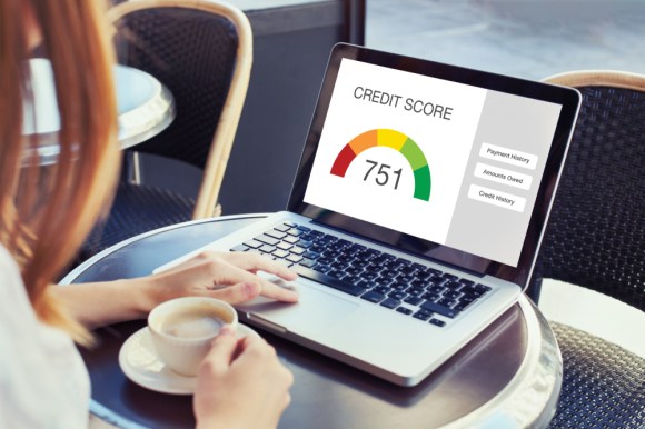 Woman checking credit report on her laptop while drinking espresso.