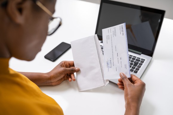 Professional Black woman opening her paycheck at her desk.