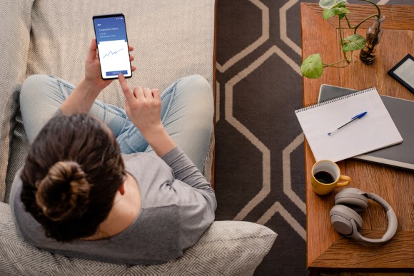 Woman sitting on the couch reviewing her investments in an app on her phone.