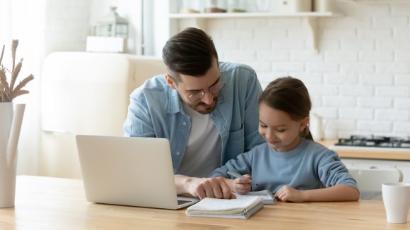 Dad sitting at the kitchen table with his child working in notebook.