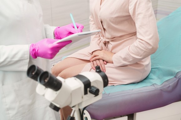 Woman wearing a hospital gown sitting on medical table.