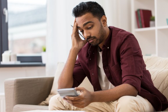 Man sitting on a couch looking confused at a calculator.