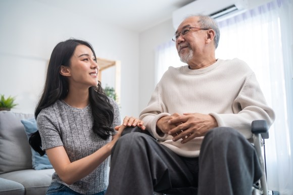 Asian woman kneeling next to an elderly Asian man in a wheelchair.