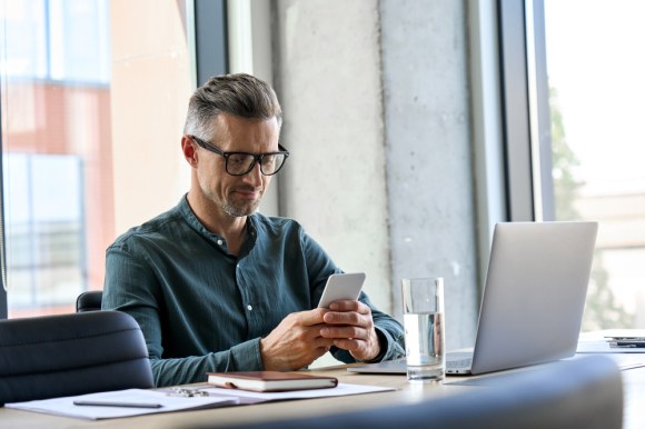 Businessman looking at his phone while sitting at his desk.