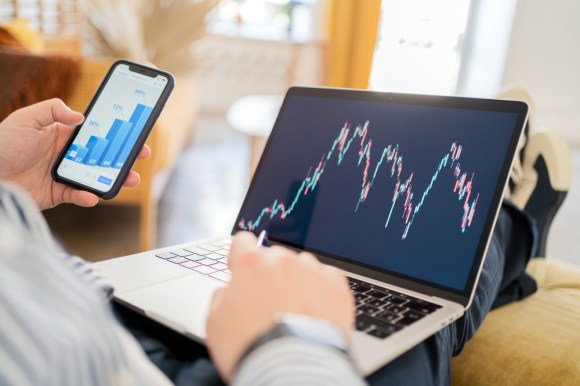 Man sitting on couch tracking investments on his laptop.