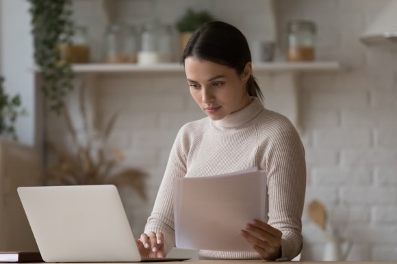 Single woman working on her laptop holding document.