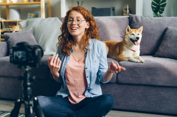 Woman filming content with her dog in the background.
