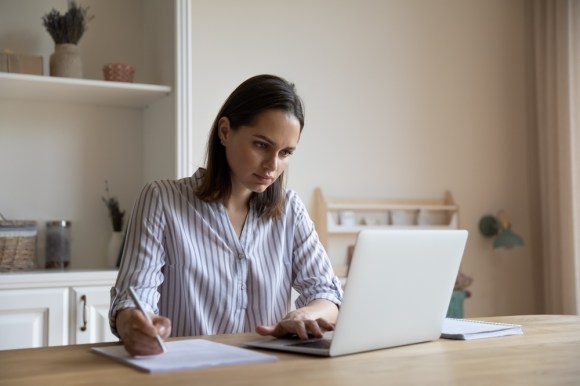 Young woman writing notes and working on her laptop.