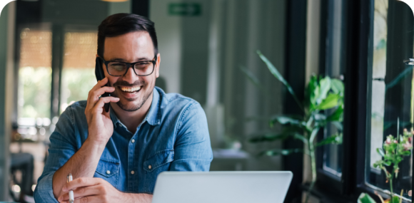 Photo of a man smiling while talking on his phone in front of his laptop