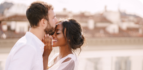 Photo of a man and woman dressed in white smiling and embracing each other