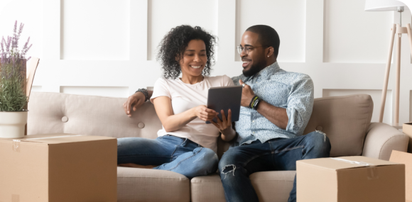 Photo of a man and woman sitting on a couch and smiling while using a tablet