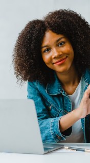 Smiling young Black woman sitting in home office using a calculator.